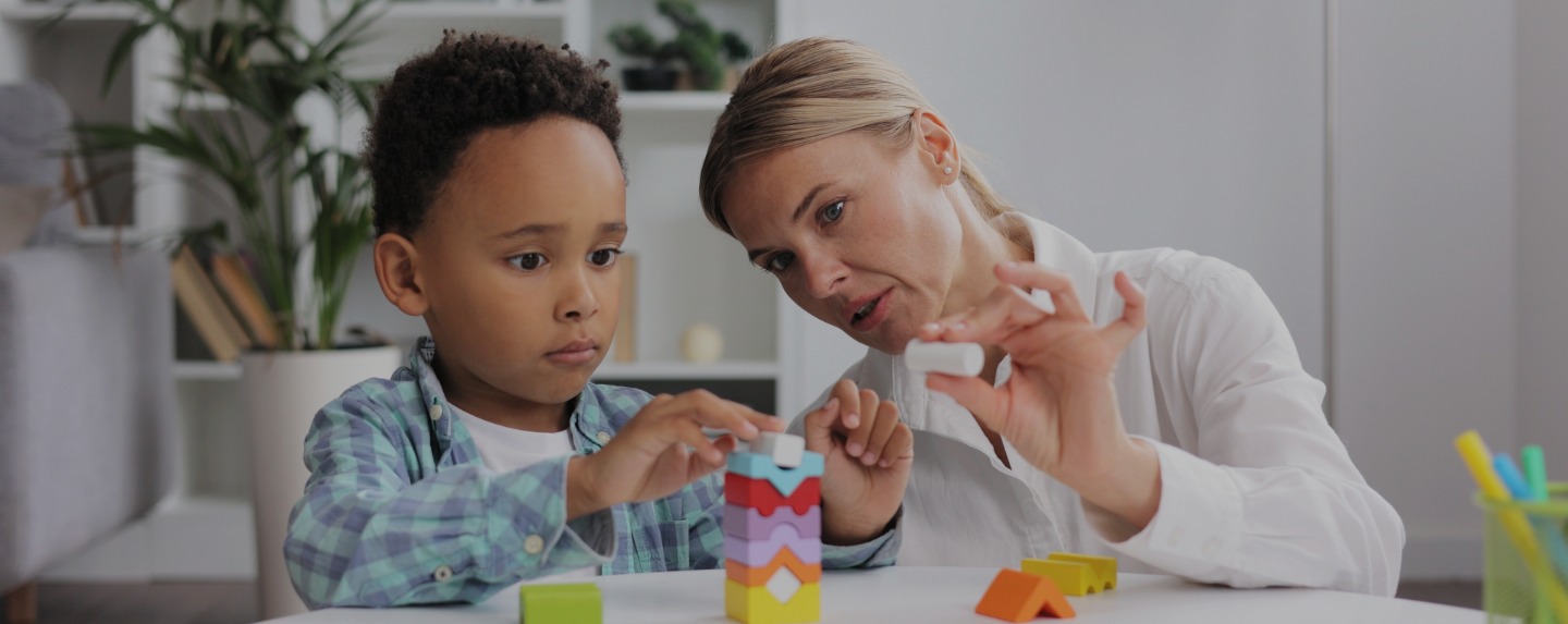 An adult and a child work together at a table in a classroom.